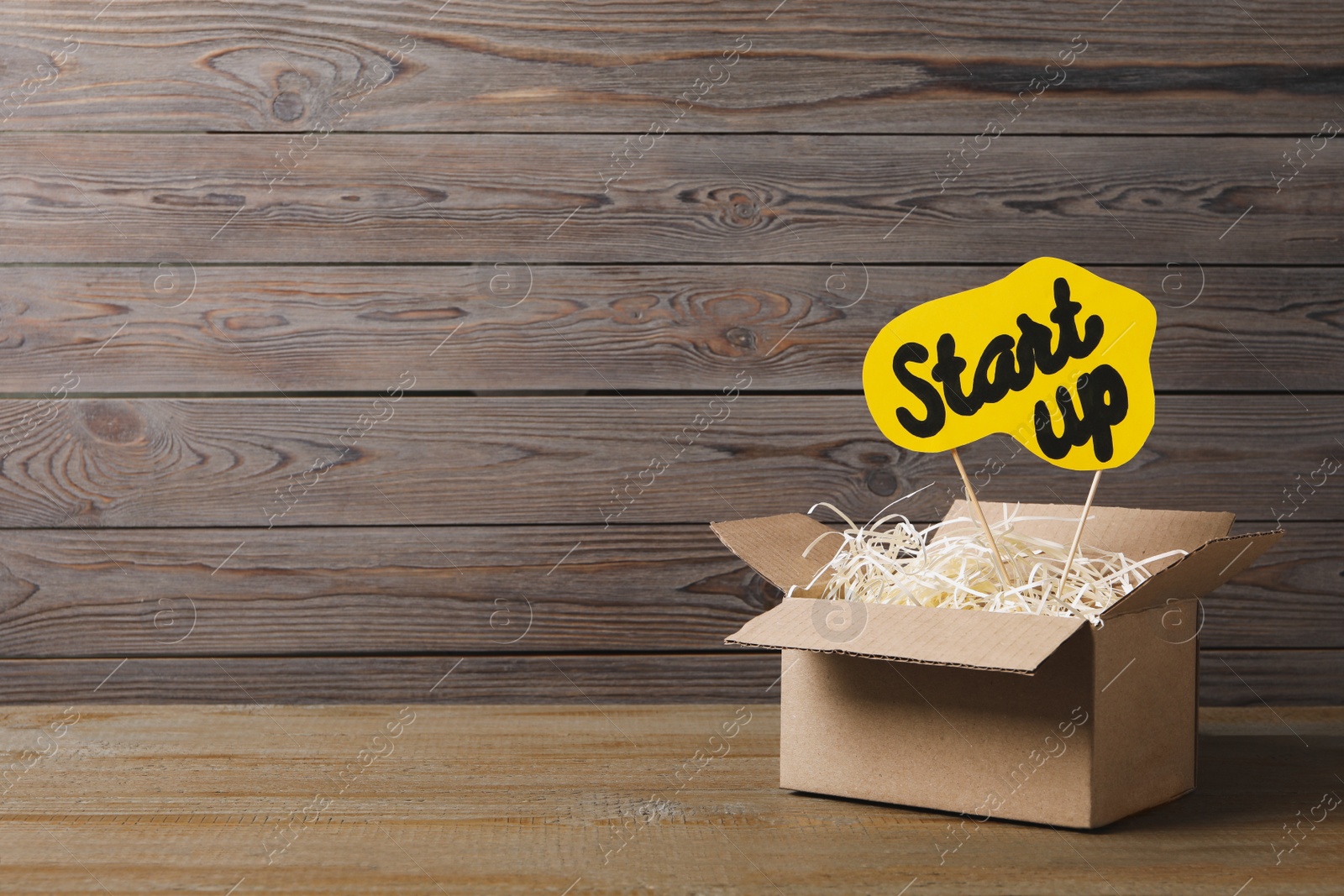 Photo of Open cardboard box and sign with words Start Up on wooden table, space for text