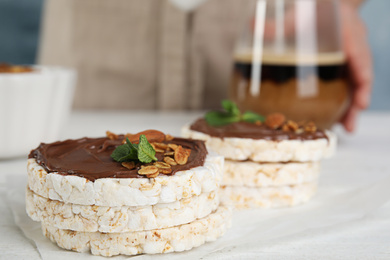 Photo of Puffed rice cakes with chocolate, nuts and mint on white wooden table, closeup. Space for text