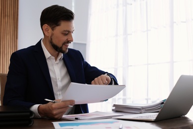 Photo of Businessman looking at wristwatch while working with documents in office