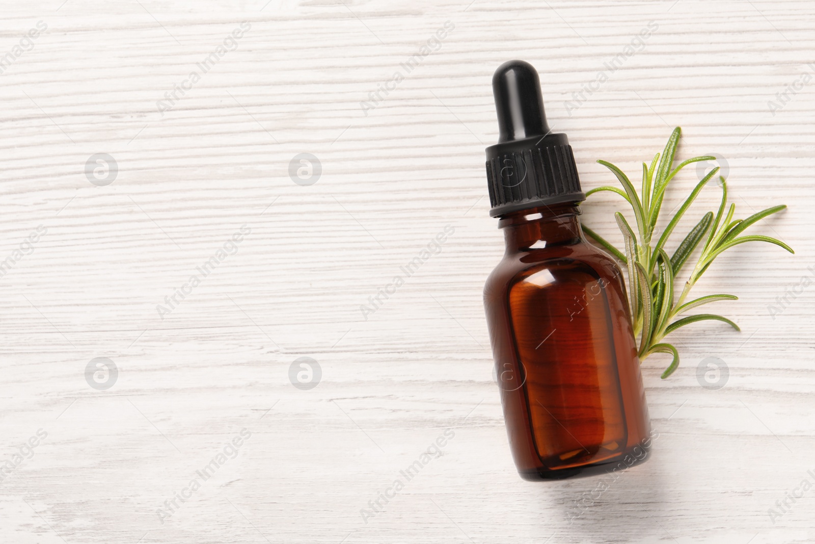 Photo of Bottle with essential oil and fresh rosemary on white wooden table, top view. Space for text