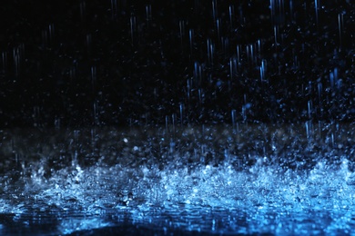 Photo of Heavy rain falling down on ground against dark background, toned in blue