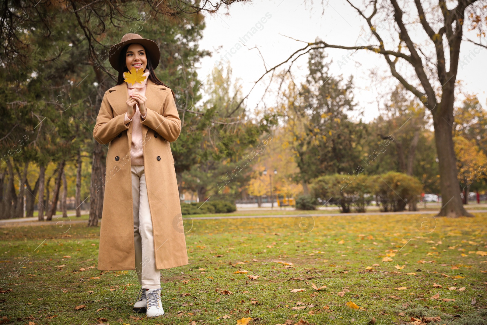 Photo of Young woman in stylish clothes holding yellow leaf outdoors, space for text. Autumn look