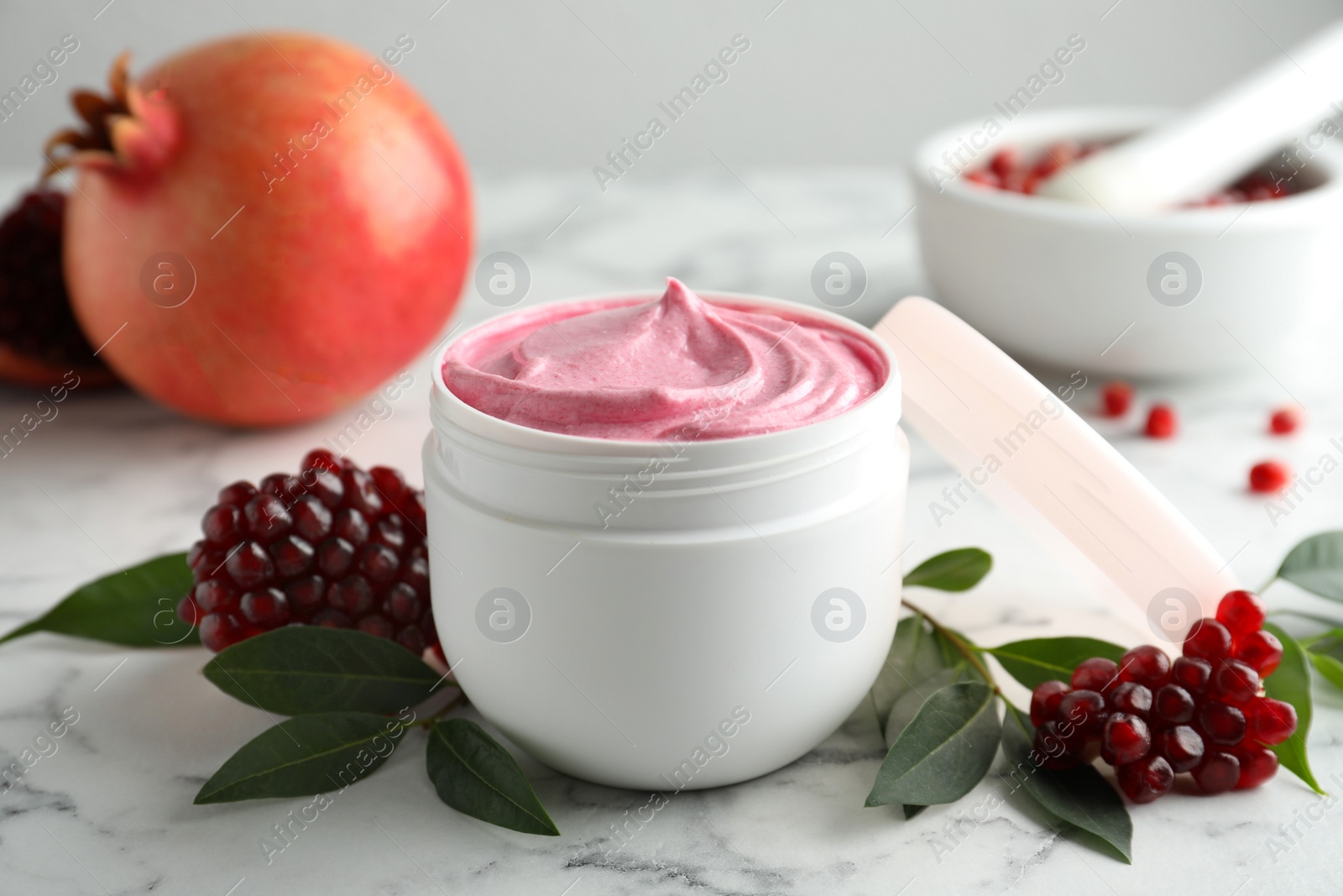 Photo of Fresh pomegranate and jar of facial mask on white marble table, closeup. Natural organic cosmetics