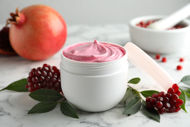 Fresh pomegranate and jar of facial mask on white marble table, closeup. Natural organic cosmetics