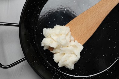 Frying pan with coconut oil and wooden spatula on light grey table, top view