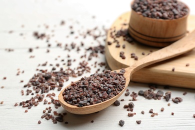 Photo of Spoon with black salt on white wooden table