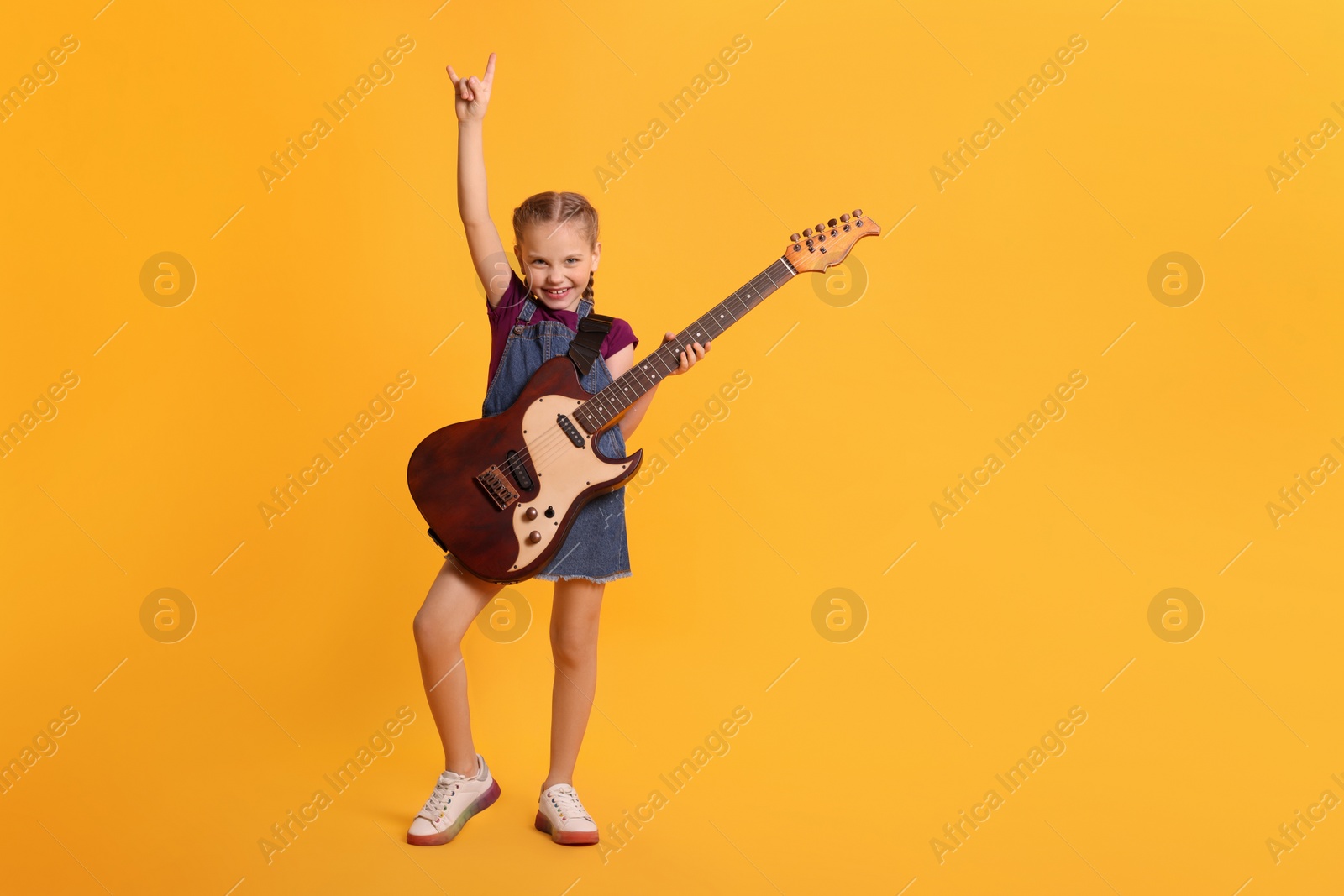 Photo of Cute girl with electric guitar on orange background