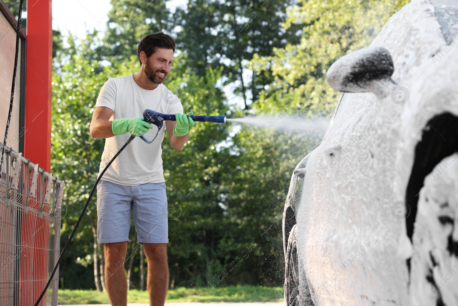 Photo of Man covering automobile with foam at outdoor car wash