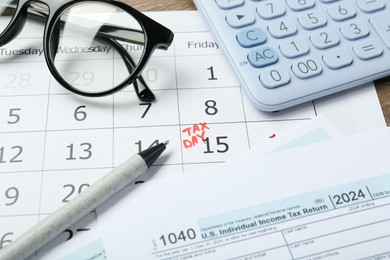 Photo of Calendar with date reminder about tax day, documents, pen, glasses and calculator on table, closeup