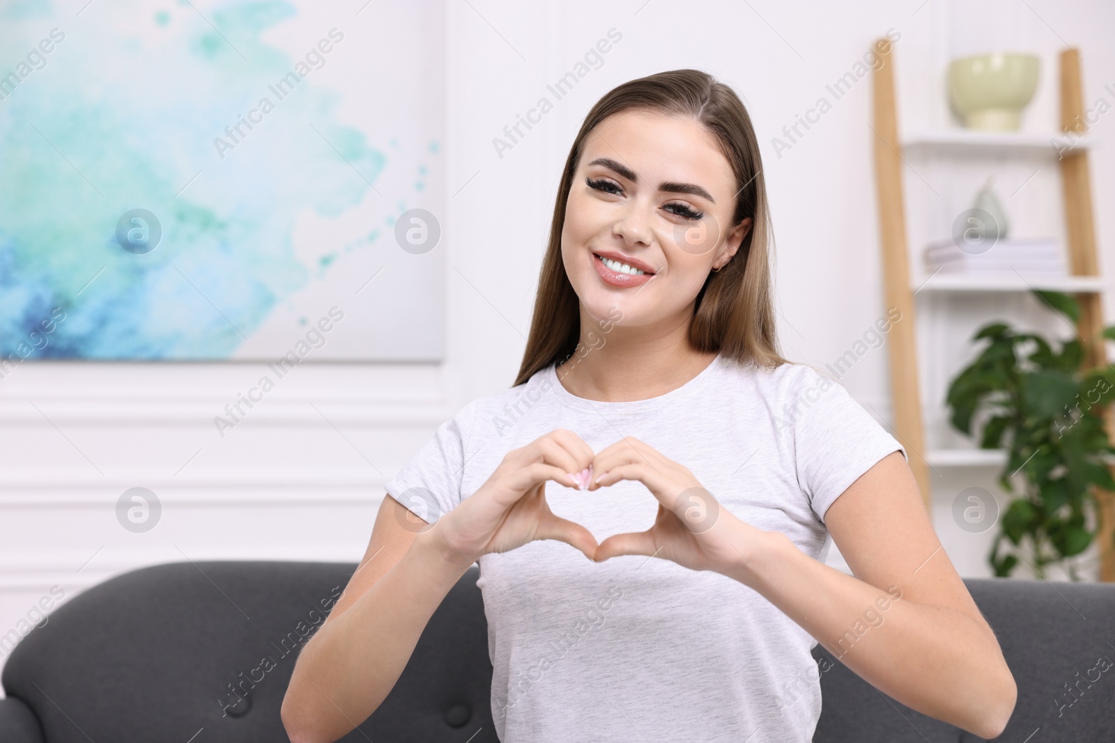 Photo of Happy woman showing heart gesture with hands at home