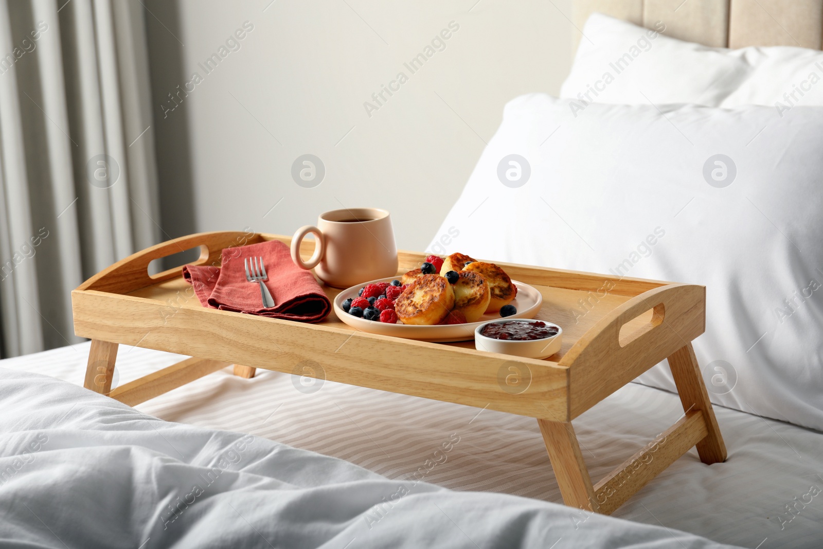 Photo of Tasty breakfast served in bedroom. Cottage cheese pancakes with fresh berries and coffee on wooden tray