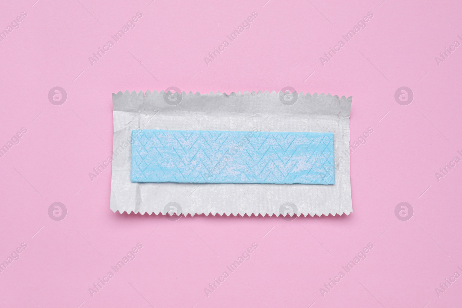 Photo of Unwrapped stick of tasty chewing gum on pink background, top view