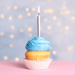 Birthday cupcake with candle on table against festive lights