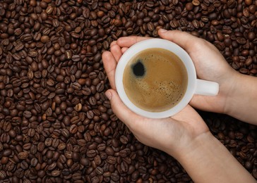 Woman with cup of tasty espresso and roasted coffee beans, top view. Space for text