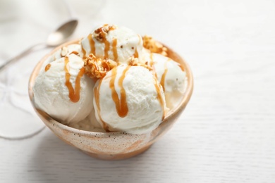 Photo of Tasty ice cream with caramel sauce and popcorn in bowl on table