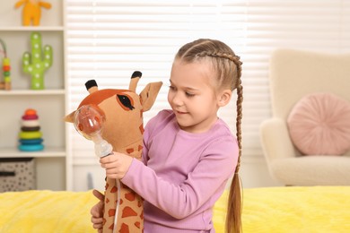 Photo of Little girl with toy giraffe and nebulizer for inhalation at home