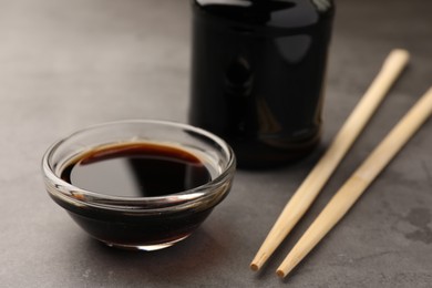 Photo of Bowl with soy sauce, chopsticks and bottle on grey table, closeup