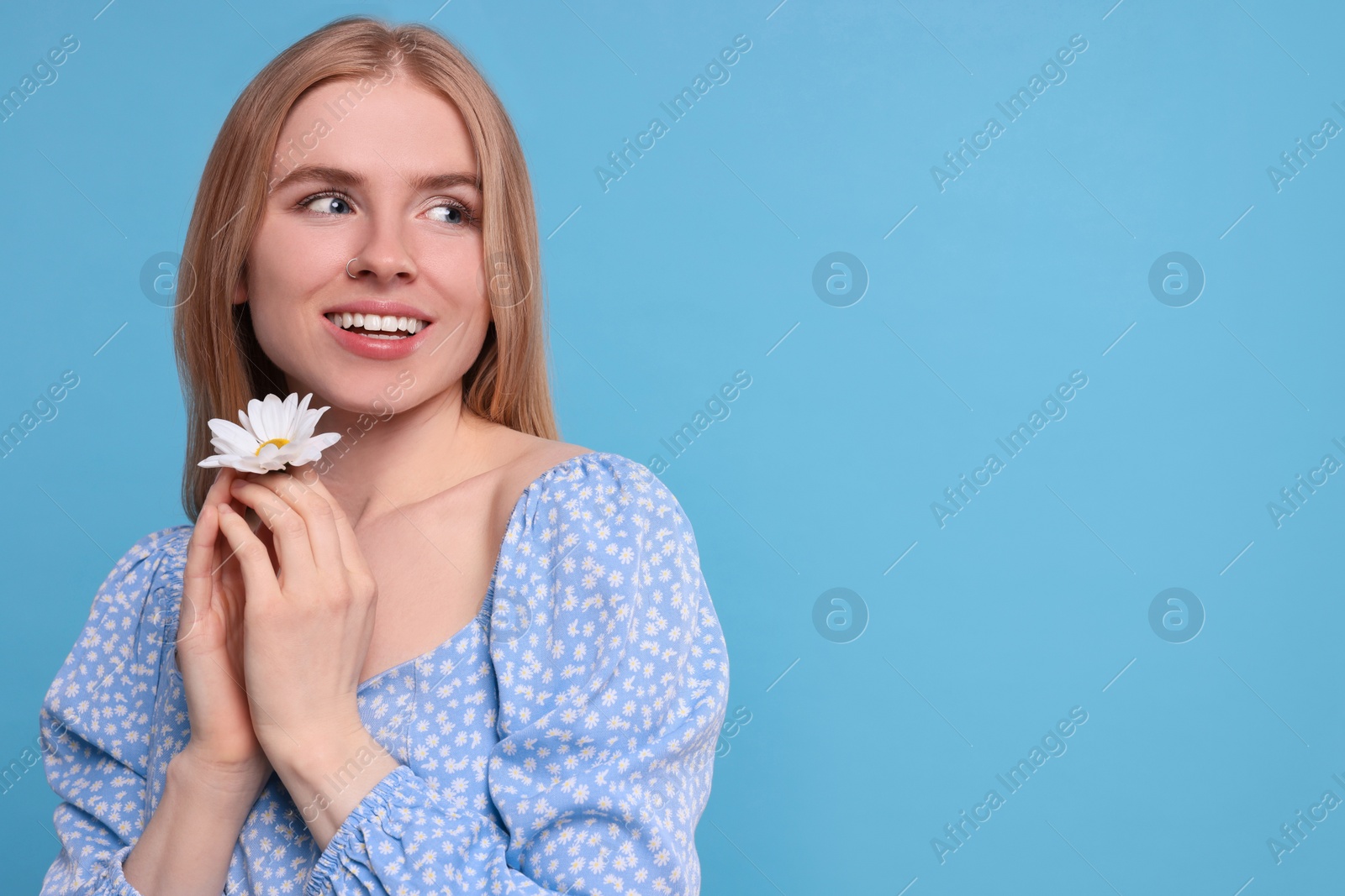 Photo of Beautiful woman with spring flower in hands on light blue background, space for text