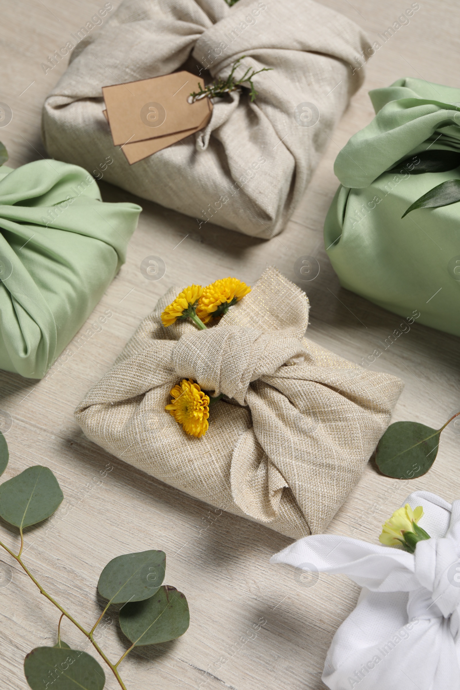 Photo of Furoshiki technique. Many gifts packed in fabric, flowers and eucalyptus leaves on wooden table