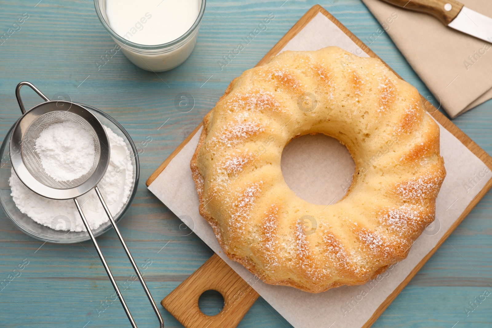 Photo of Delicious sponge cake with powdered sugar and glass of milk on light blue wooden table, flat lay