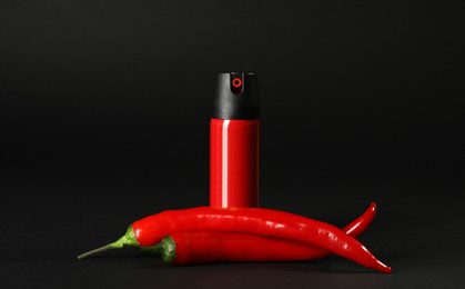 Photo of Bottle of gas pepper spray and fresh chili peppers on black background