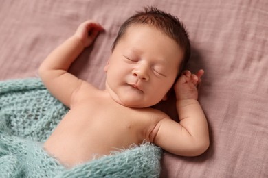 Adorable newborn baby in turquoise knitted blanket sleeping on bed