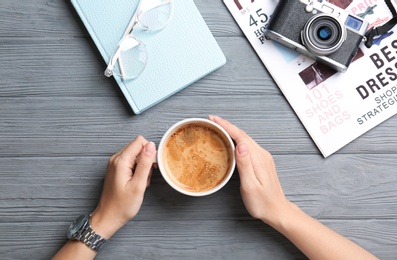 Photo of Young woman with cup of delicious coffee at table, top view