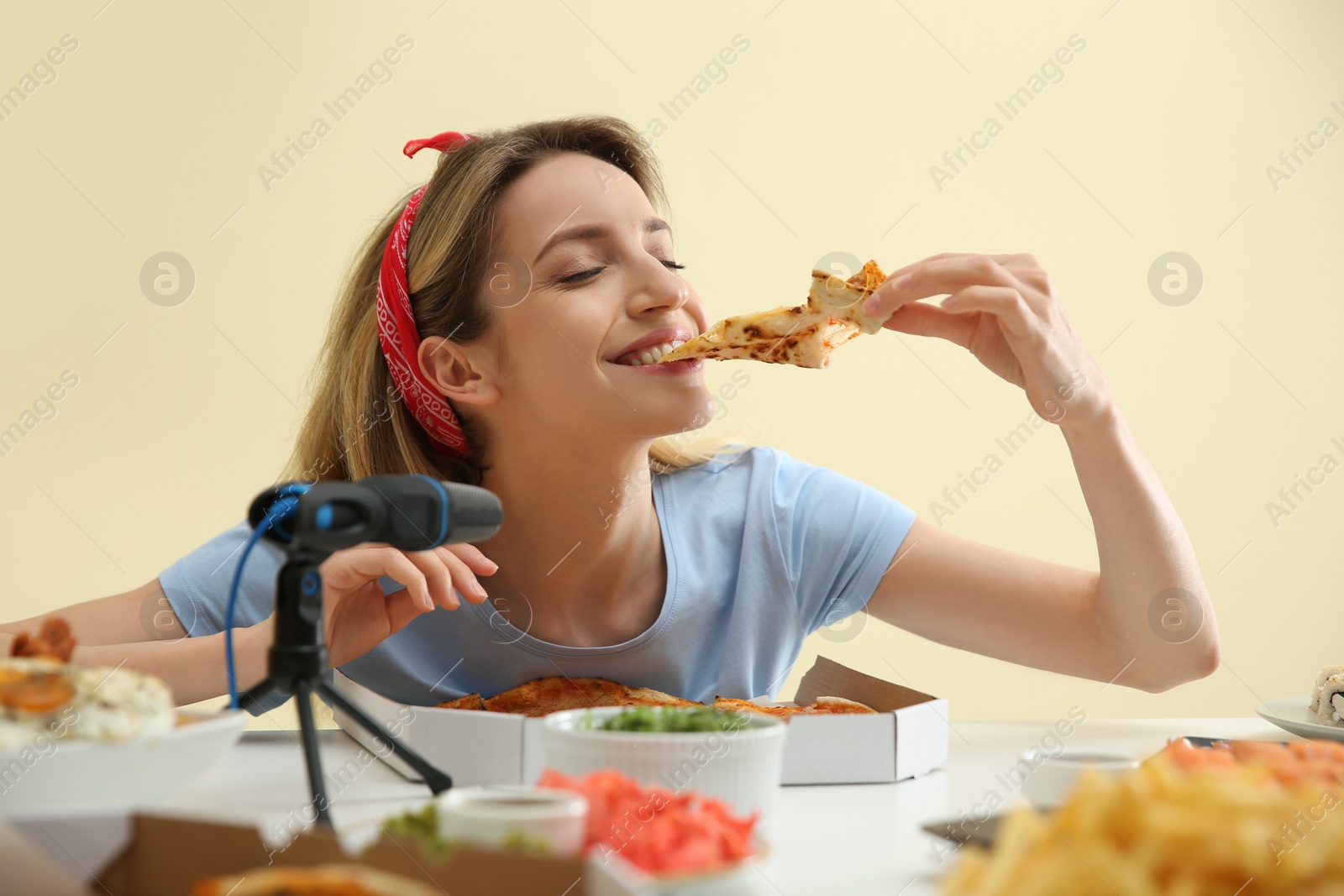 Photo of Food blogger eating in front of microphone at table against light background. Mukbang vlog