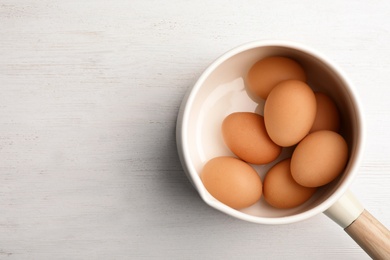 Photo of Saucepan with boiled eggs on wooden background, top view. Space for text