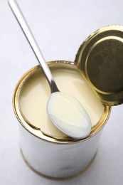 Photo of Open tin can with condensed milk and spoon on white table, closeup