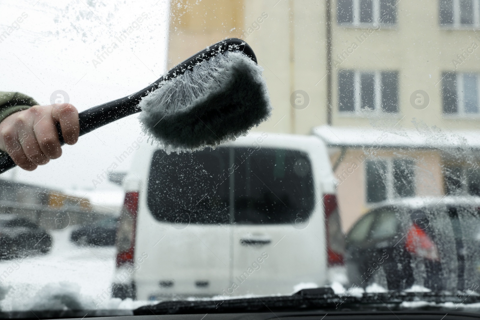 Photo of Closeup of woman cleaning windshield from snow with brush, view from inside