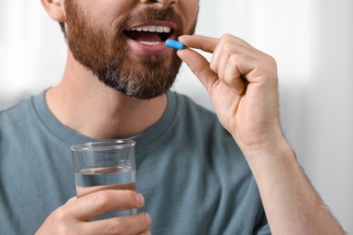 Photo of Man with glass of water taking pill on blurred background, closeup