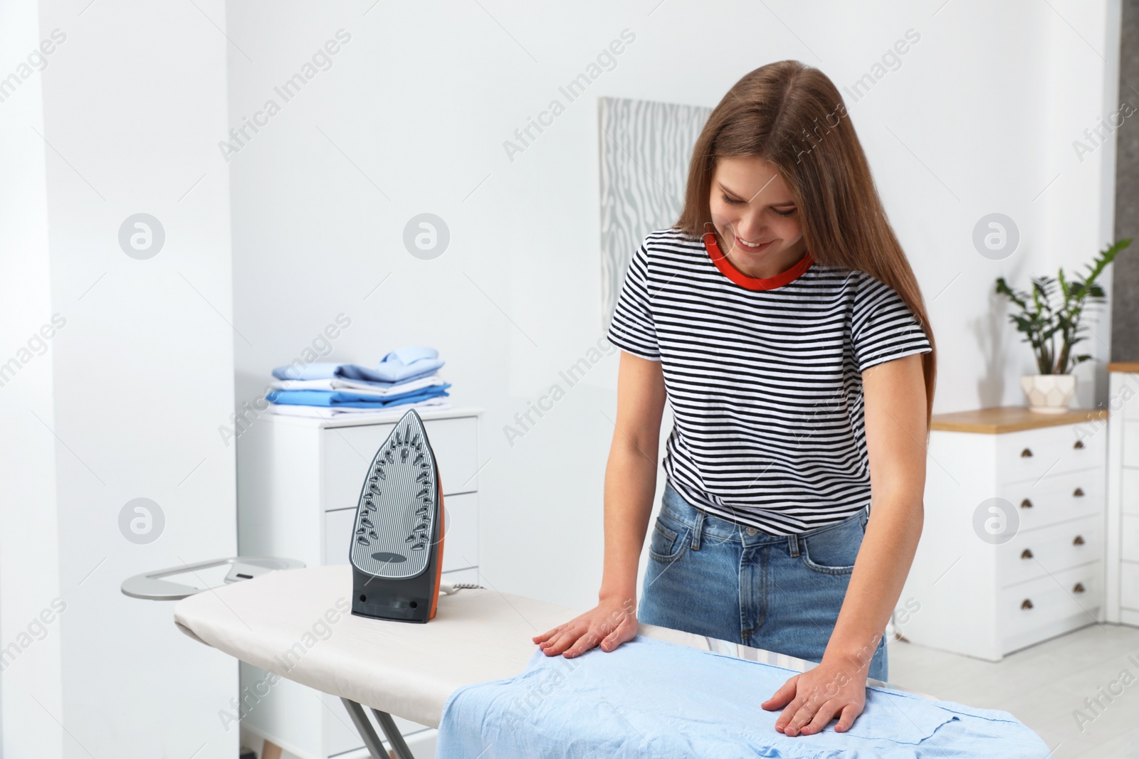 Photo of Young woman ironing clothes on board at home