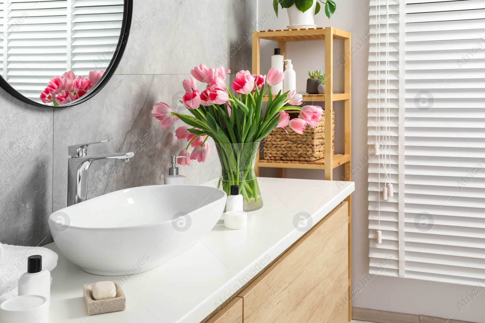 Photo of Vase with beautiful pink tulips and toiletries near sink in bathroom