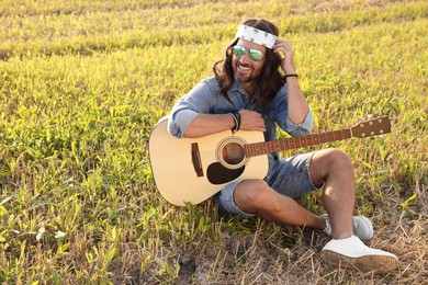 Photo of Happy hippie man with guitar in field, space for text