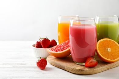 Wooden board with different juices and fresh fruits on table. Space for text