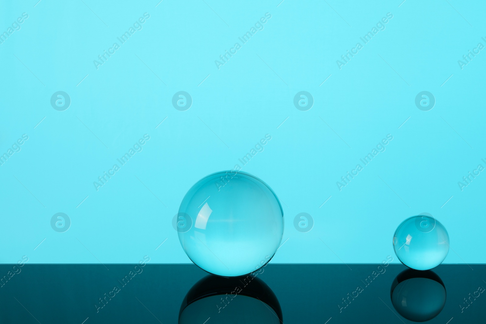 Photo of Transparent glass balls on mirror surface against turquoise background. Space for text