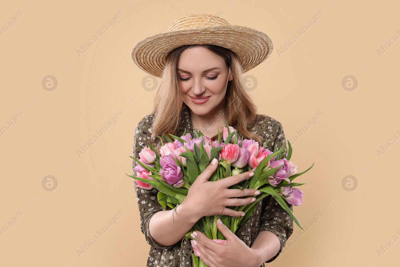 Photo of Happy young woman in straw hat holding bouquet of beautiful tulips on beige background