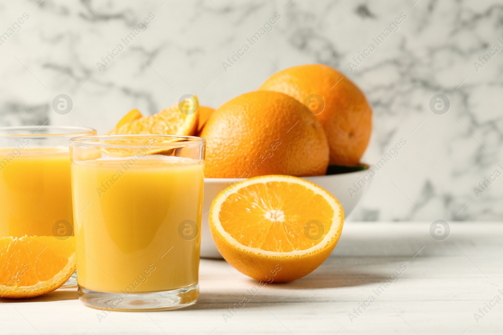 Photo of Glasses of orange juice and fresh fruits on white wooden table