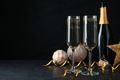 Happy New Year! Bottle of sparkling wine, glasses and festive decor on black background, space for text