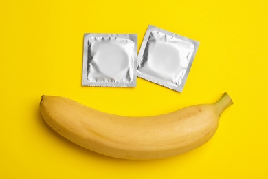 Photo of Condoms and banana on yellow background, flat lay. Safe sex