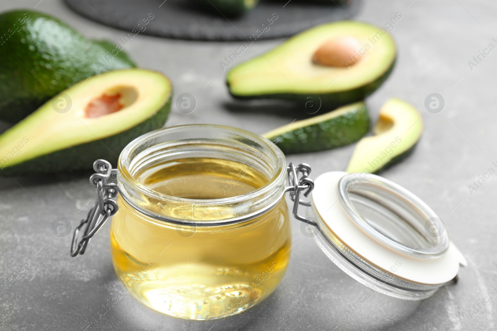 Photo of Jar of natural oil and avocados on grey stone background