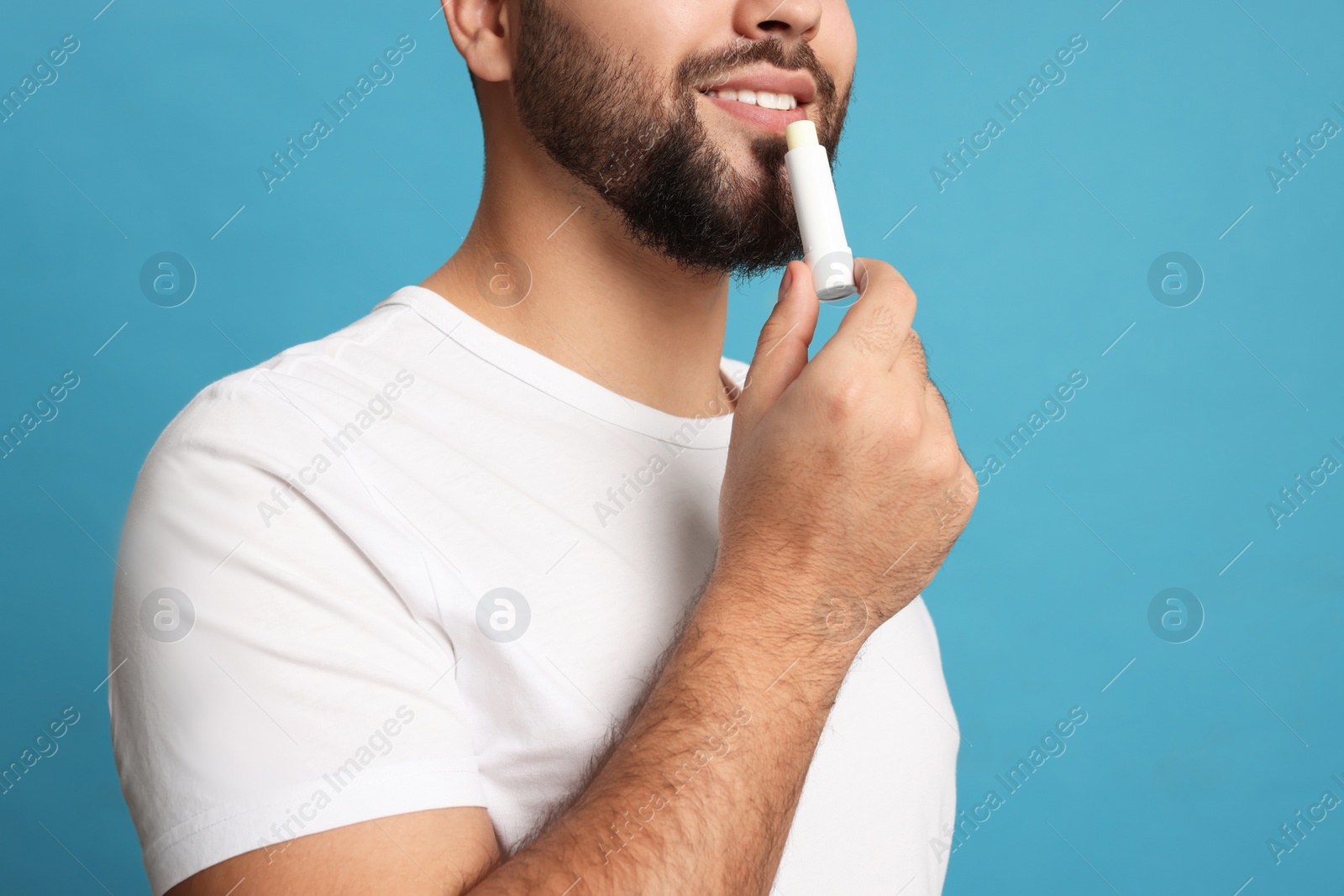 Photo of Young man applying lip balm on turquoise background, closeup