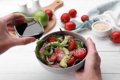 Woman adding soy sauce to tasty salad at white wooden table, closeup