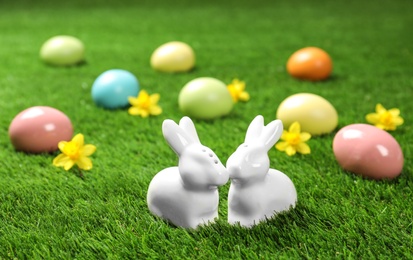 Photo of Ceramic Easter bunnies and dyed eggs on green grass