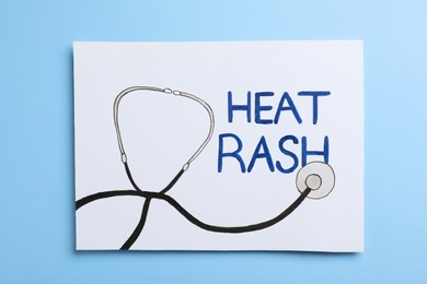 Photo of Sheet of paper with words Heat Rash and drawn stethoscope on light blue background, top view
