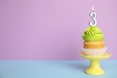 Photo of Birthday cupcake with number three candle on stand against color background, space for text