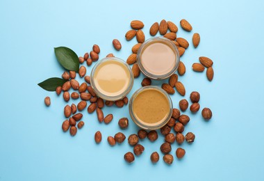 Different types of delicious nut butters and ingredients on light blue background, flat lay