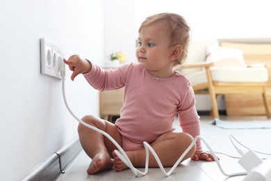 Photo of Cute baby playing with electrical socket and plug at home. Dangerous situation