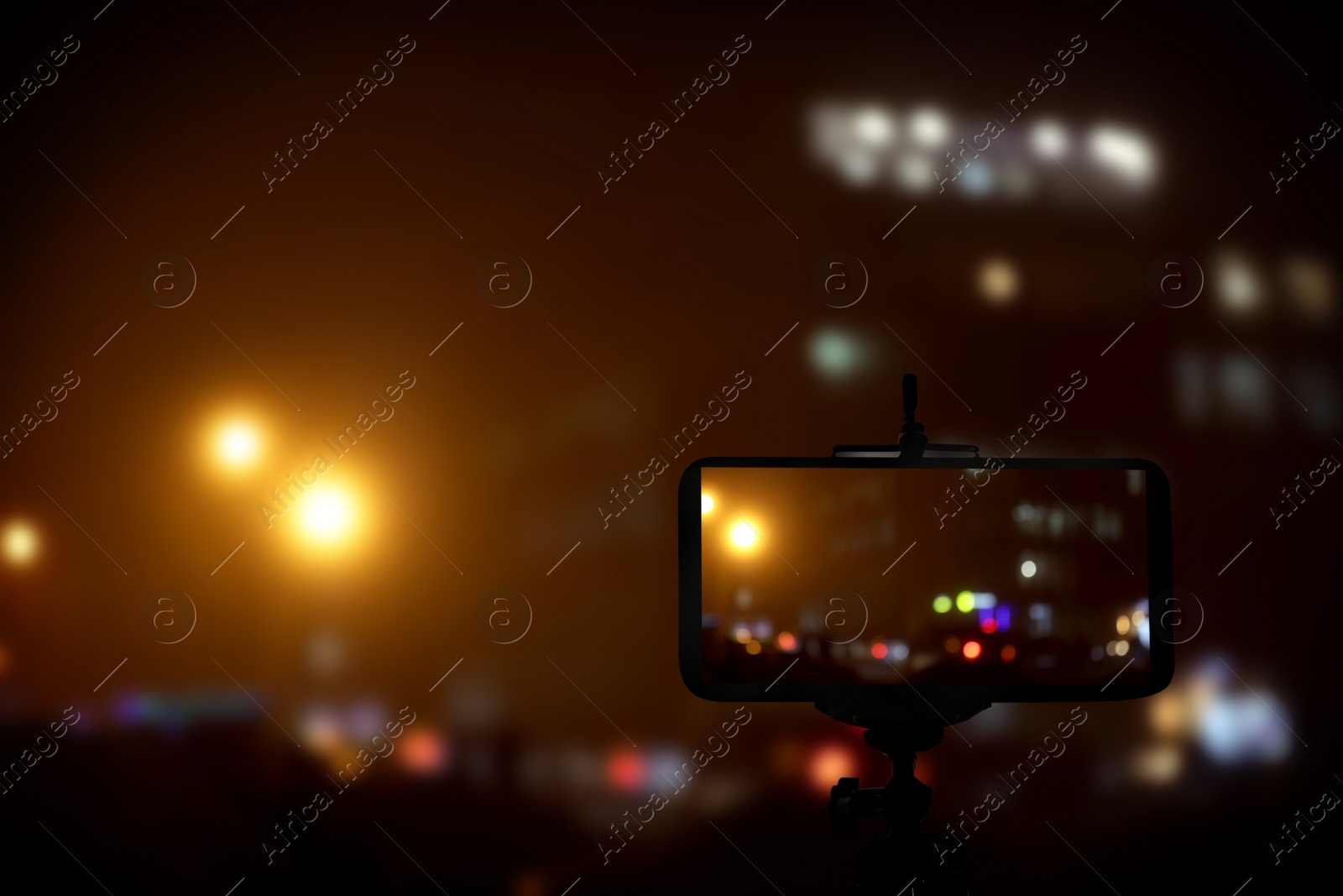 Image of Taking photo of with smartphone mounted on tripod. Blurred view of city lights at night, bokeh effect